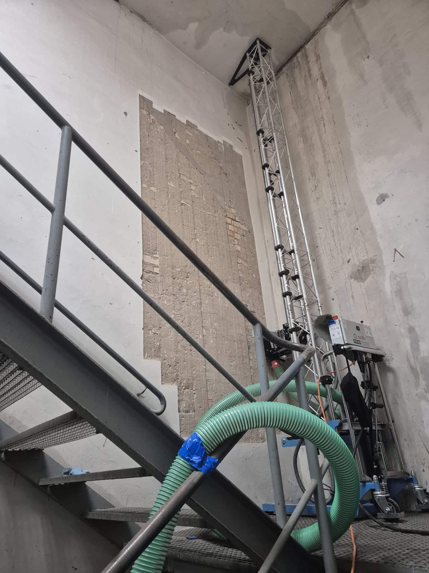 Treppenhaus eines Industriegebäudes mit teilweise abgetragenem asbesthaltigem Wandputz und Absaugtechnik