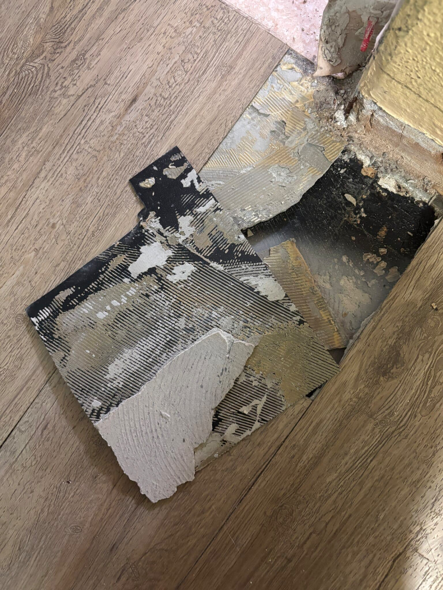 Entferntes PVC-Belagstück mit asbesthaltigem Kleber auf Holzfußboden während der Sanierung